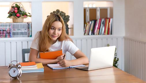 年轻的女学生坐在桌子前用笔记本电脑工作